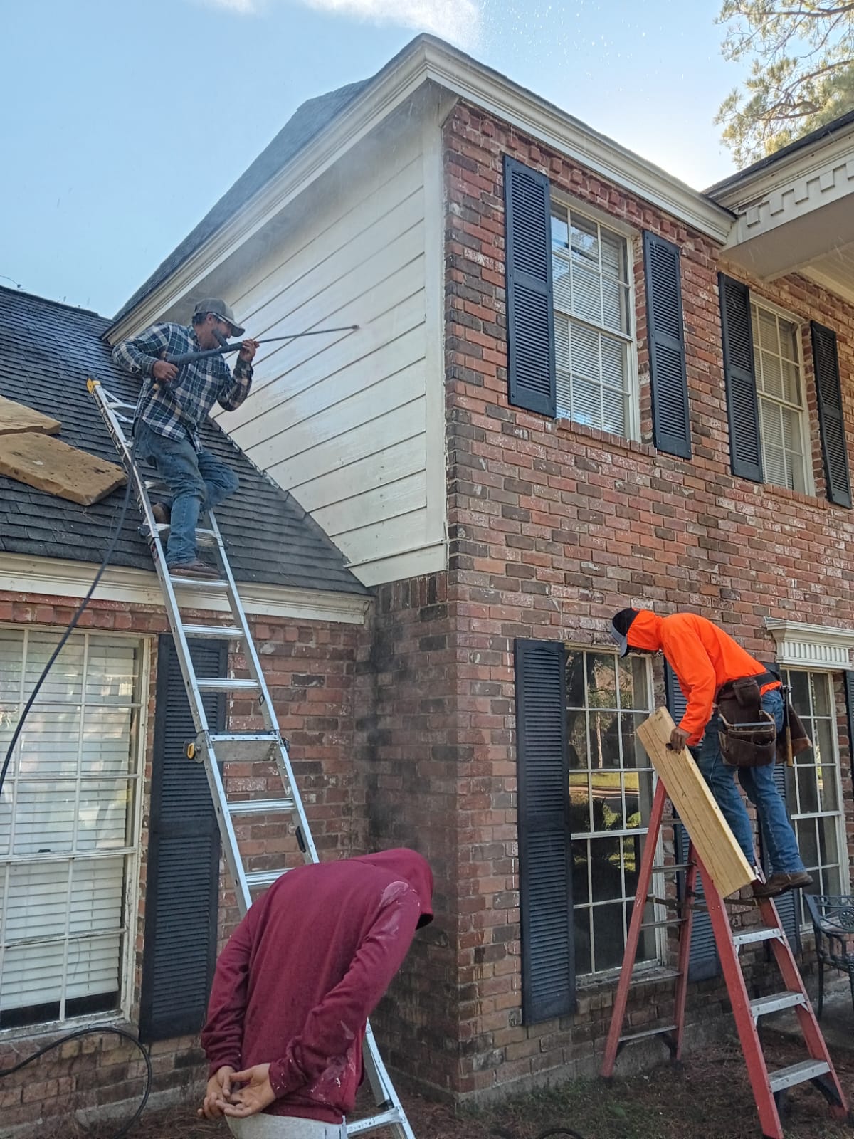 Two men working on the exterior of a brick house using ladders.