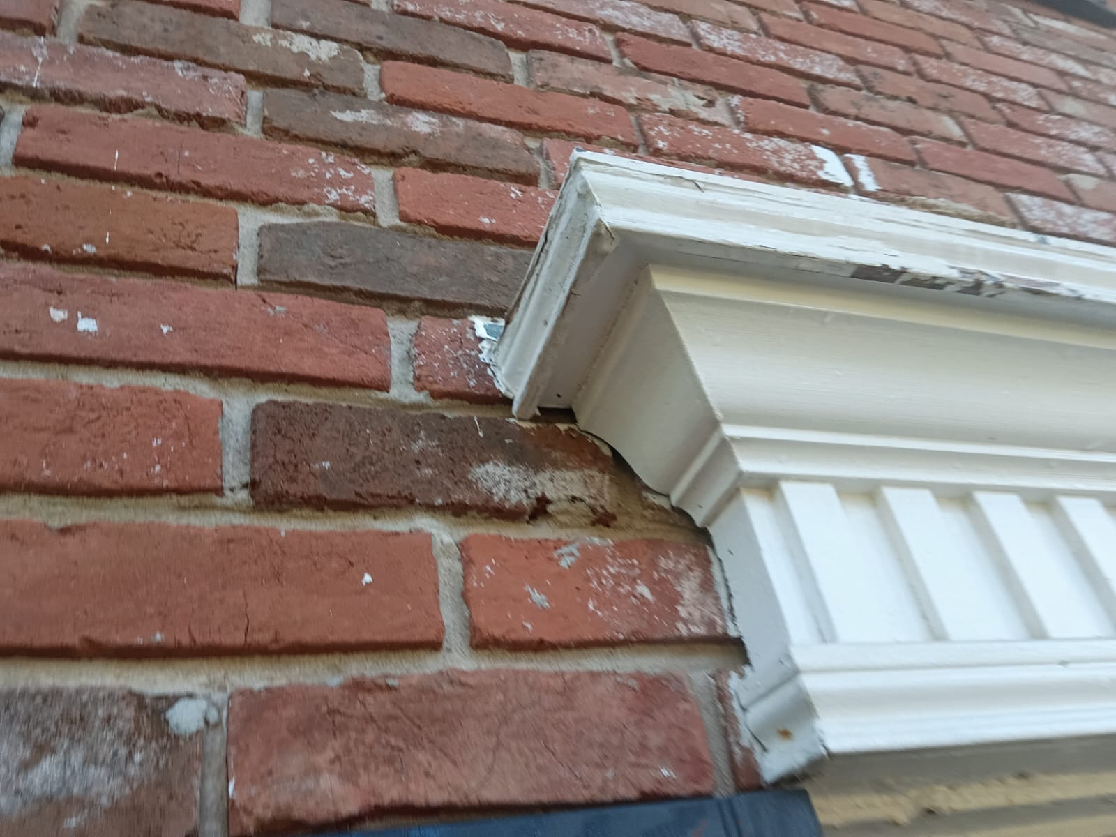 Close-up of brick wall with damaged mortar near white decorative molding.
