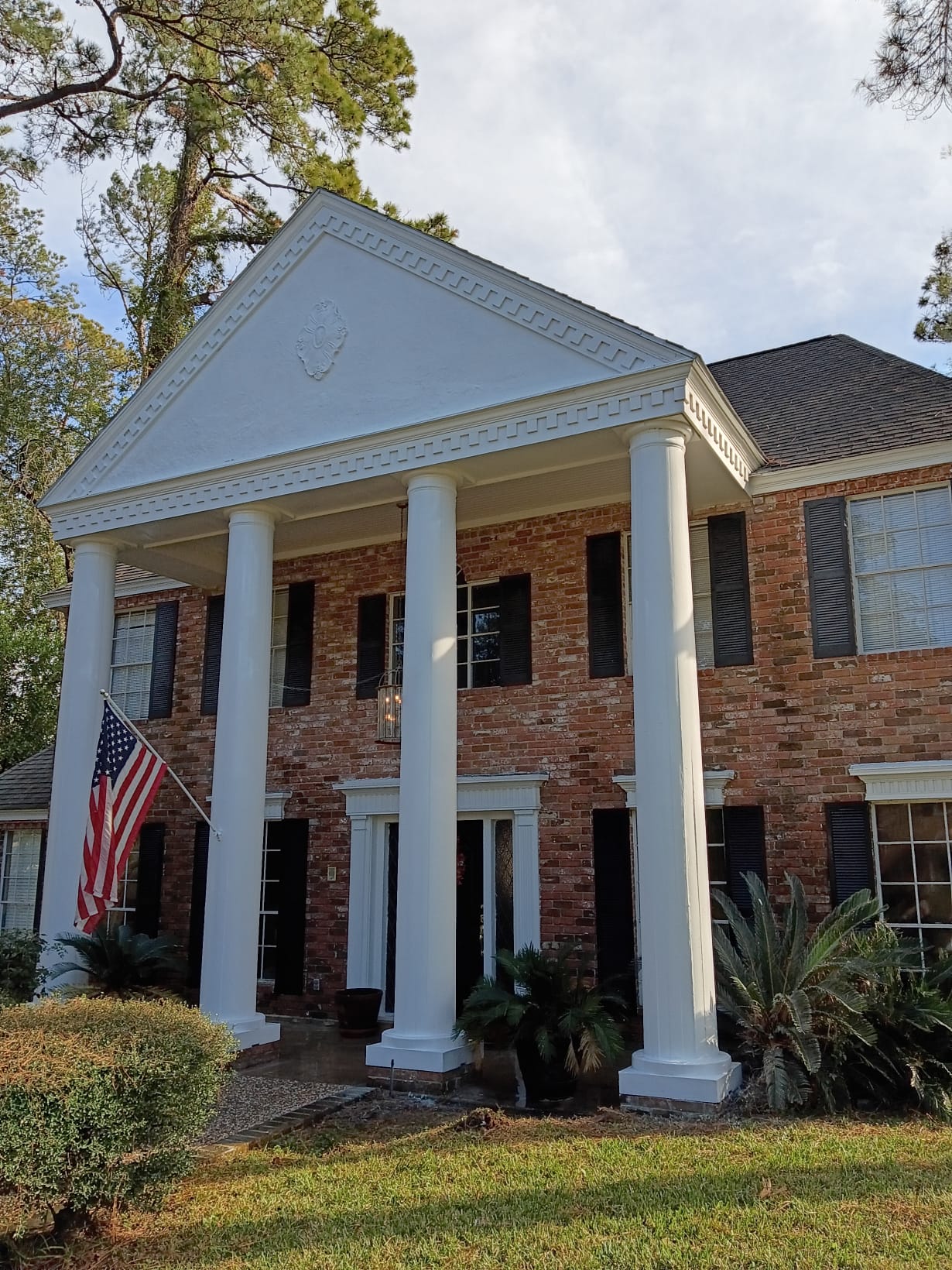 A brick house with tall white columns and an American flag.