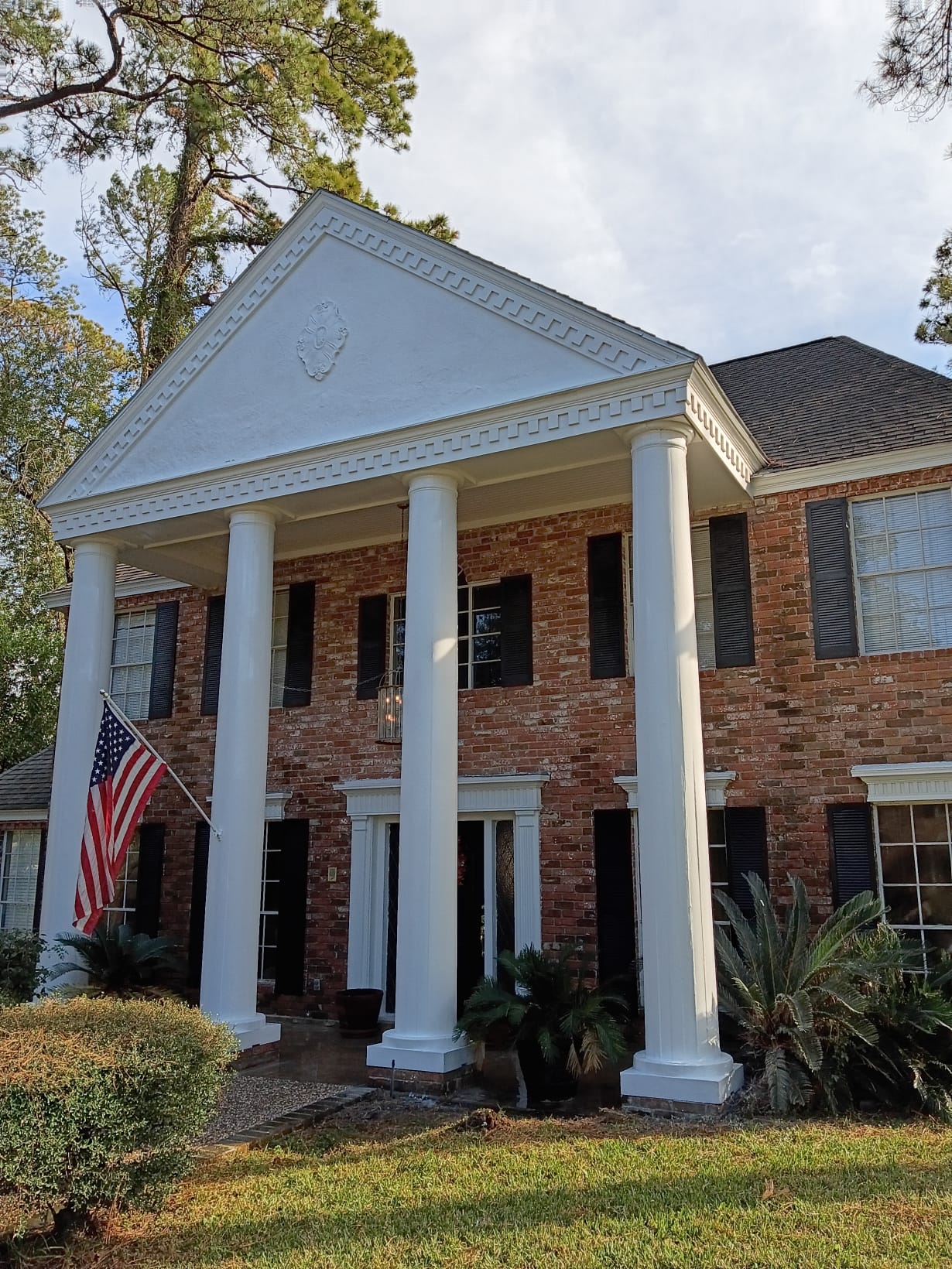 Front view of a brick house with large white columns and an American flag.