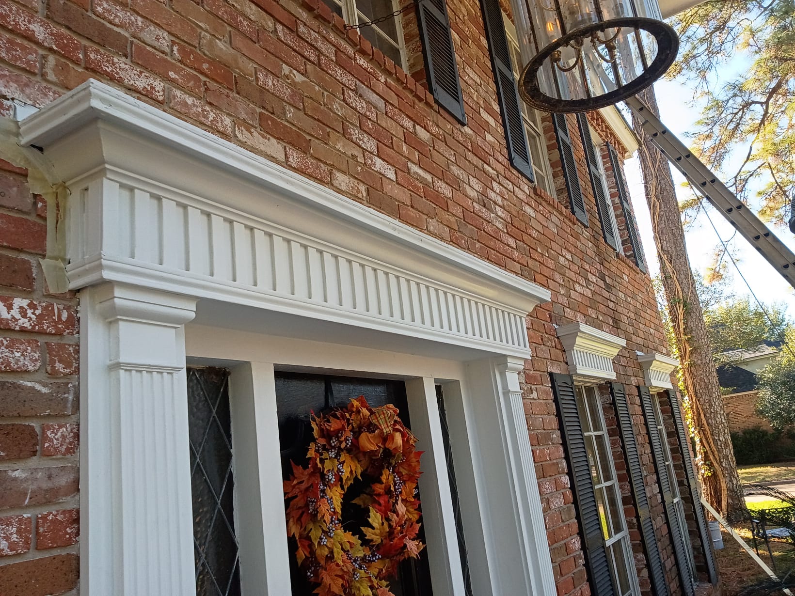 Front door decorated with a fall-themed wreath on a brick house.