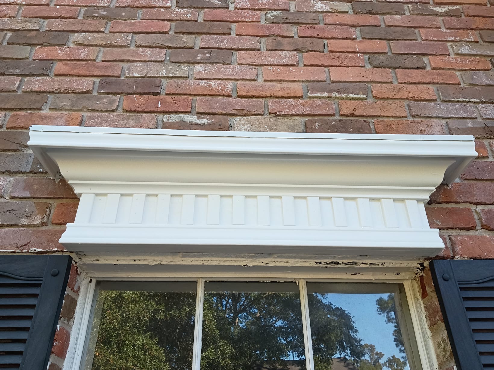 A white decorative molding above a window on a brick wall.