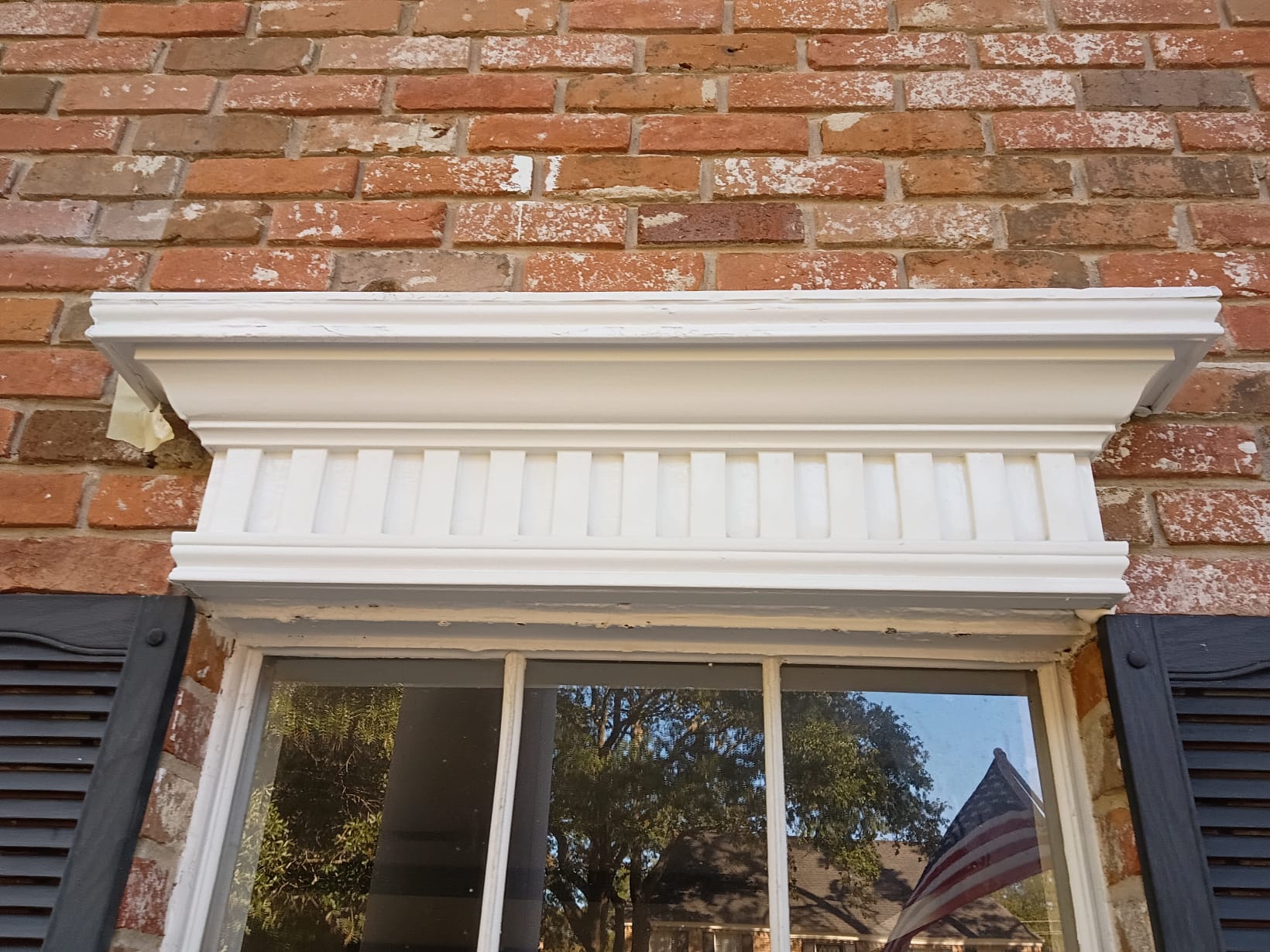 Decorative white molding above a window on a brick house.