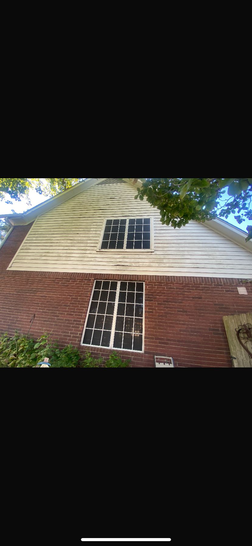 Two-story house with brick and white siding under tree shade.