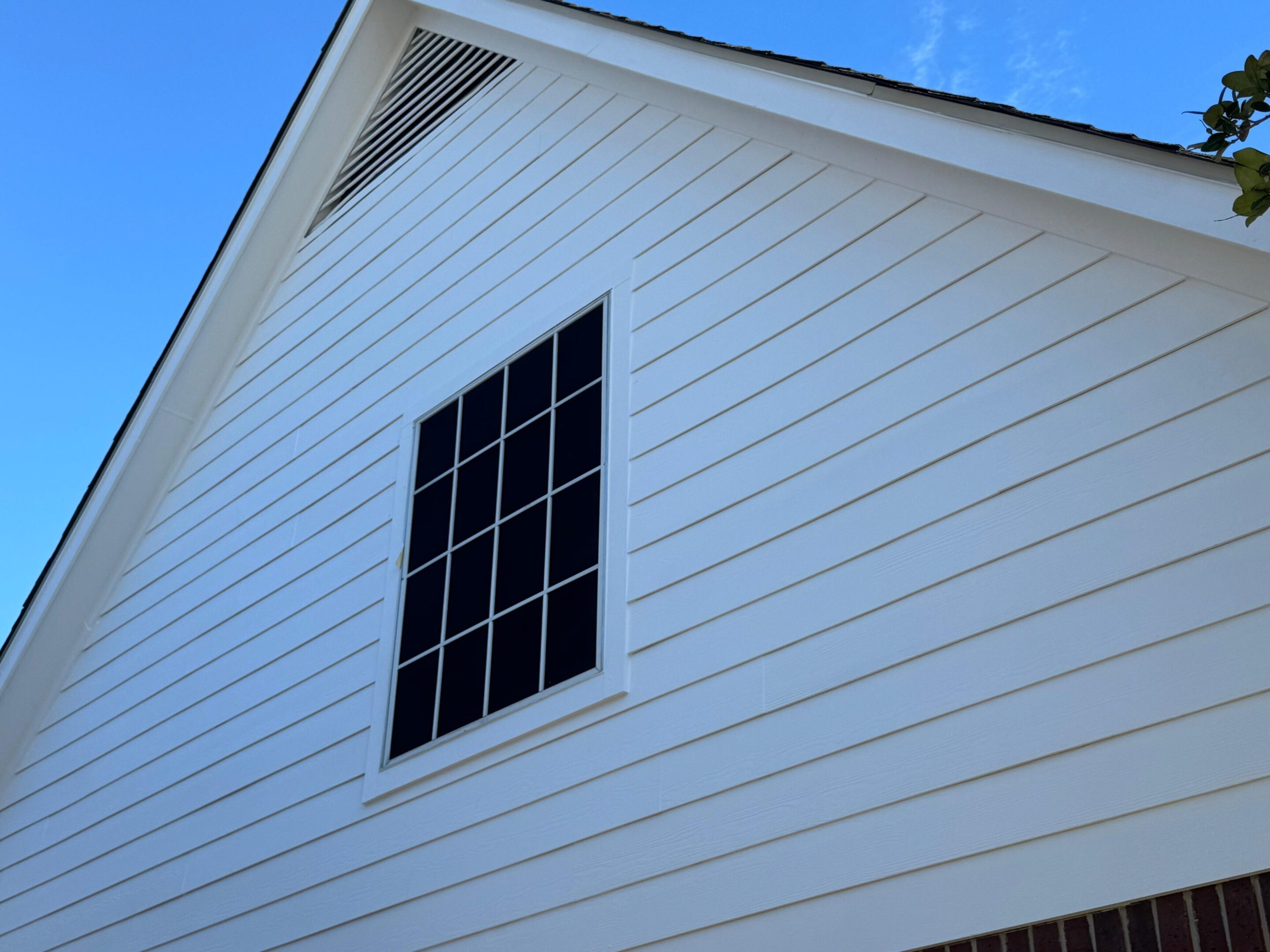 White wooden house siding with a black window frame under a clear blue sky.