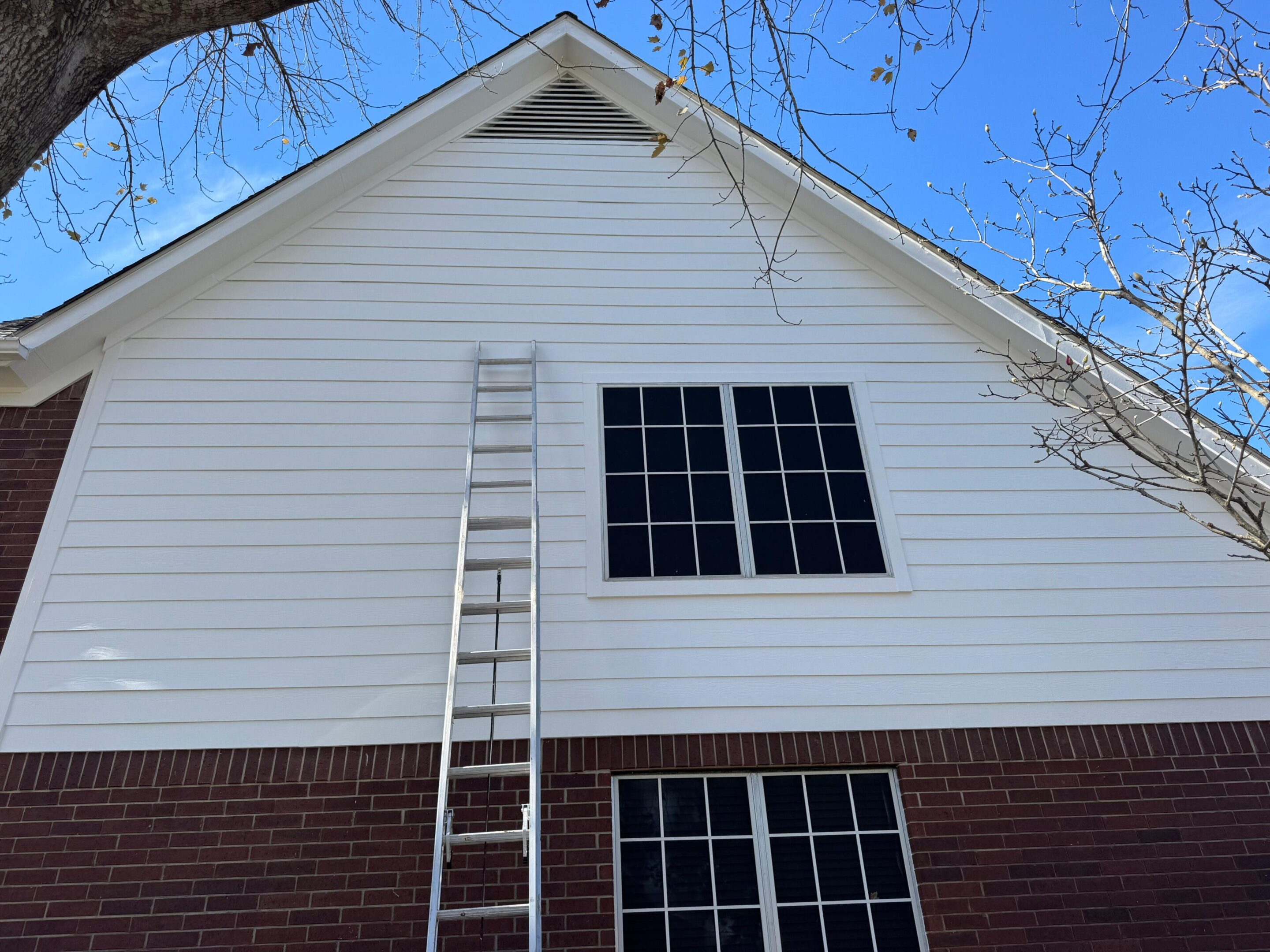 A tall ladder leaning against a white and brick two-story house under a clear blue sky.