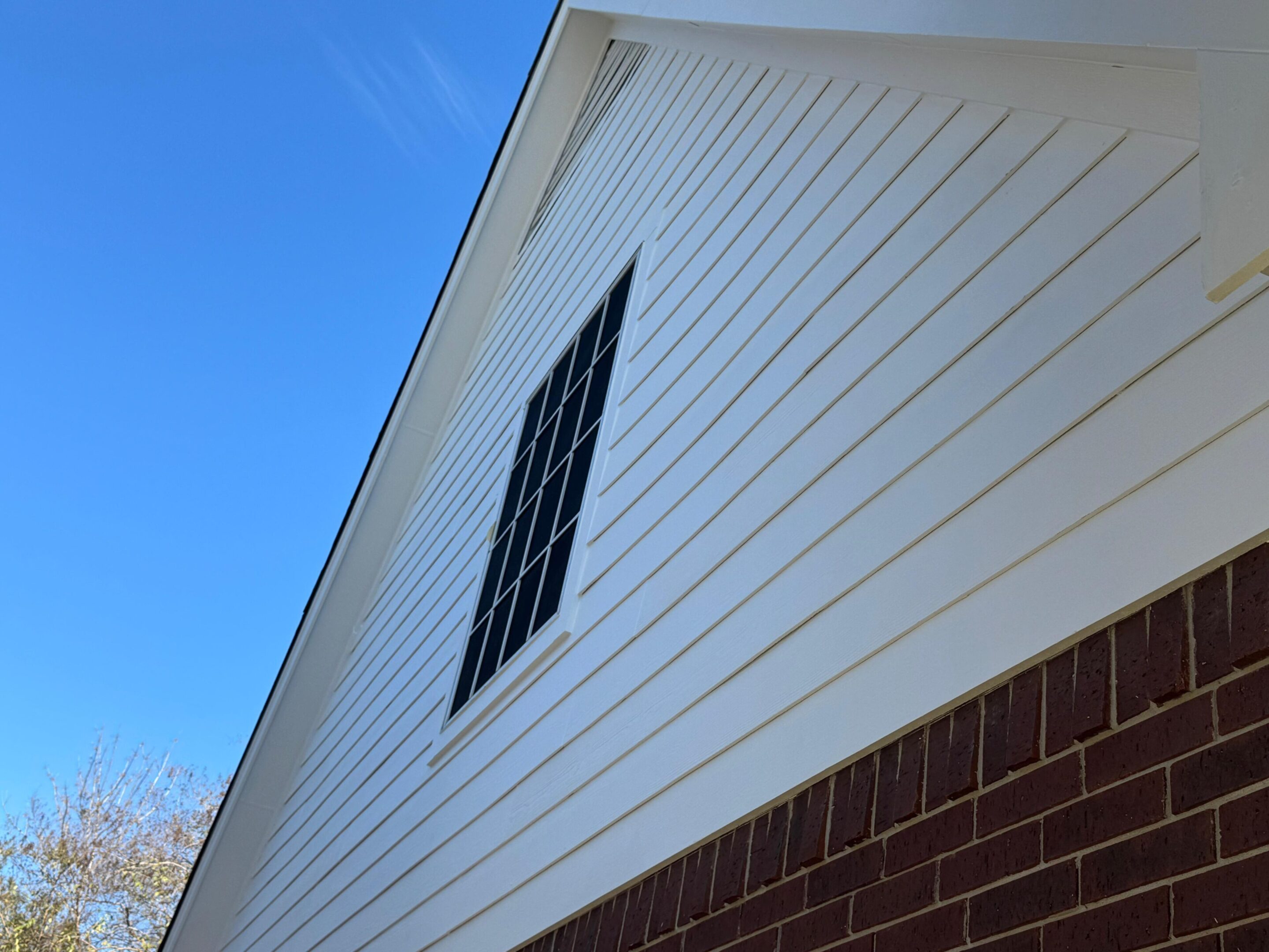 White siding on a building's upper wall with a barred window and blue sky.