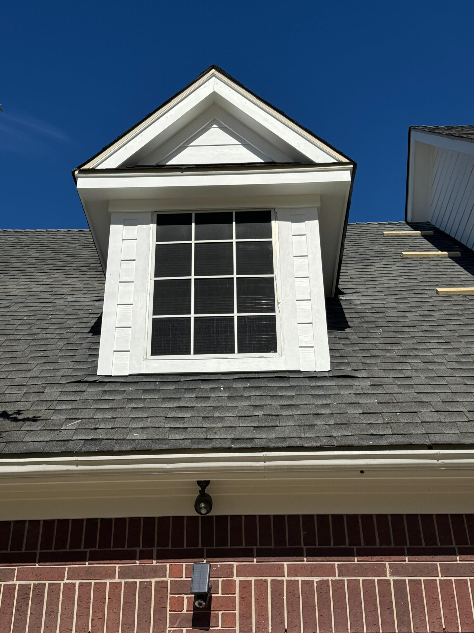 Dormer window on a gray shingled roof under a clear blue sky.