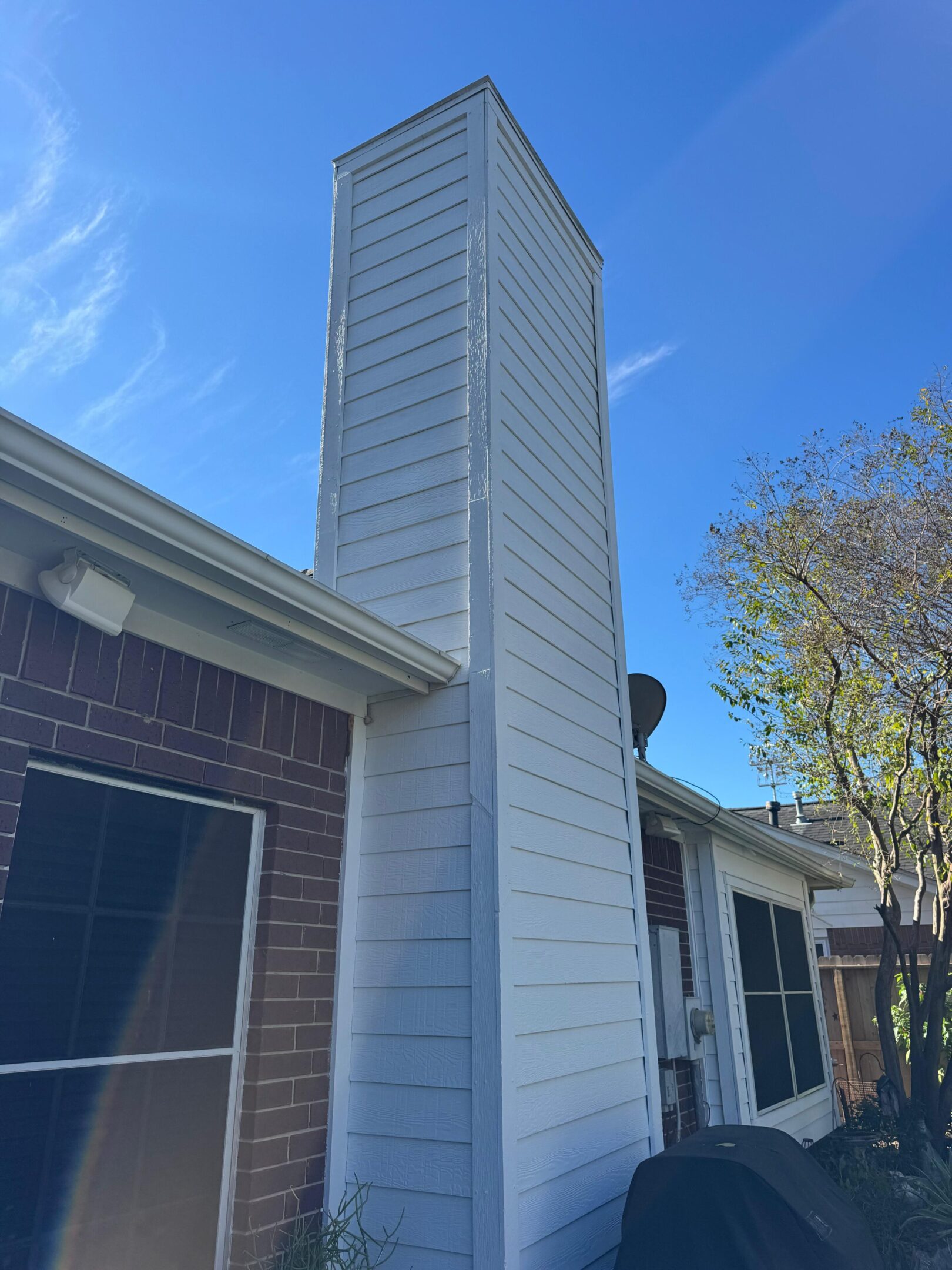 Tall chimney attached to a house under clear blue sky.