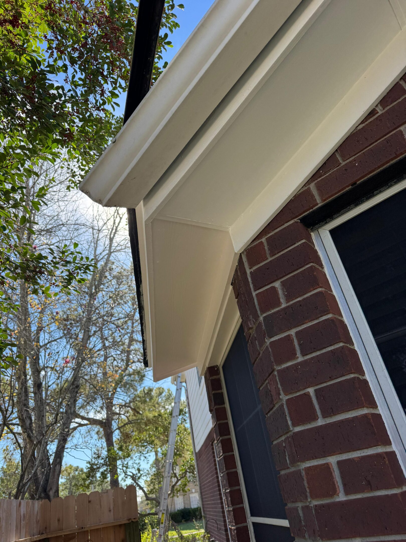 Close-up of a house roof corner with gutter and brick wall under a blue sky.