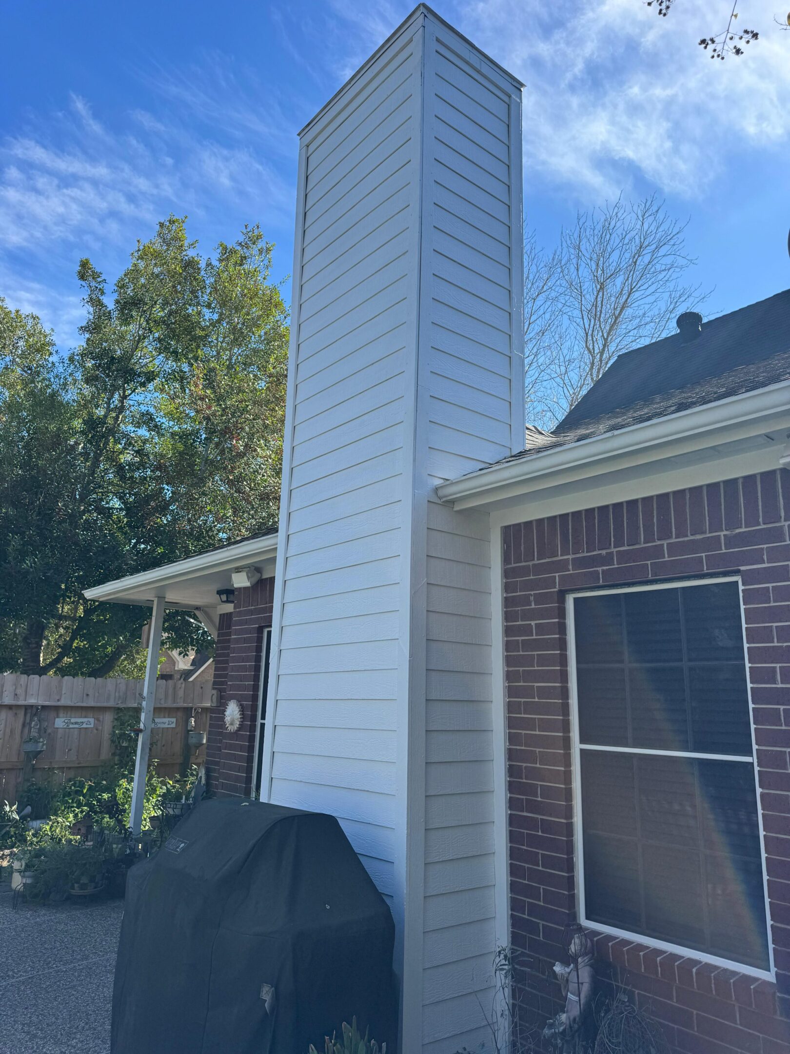 Tall white chimney attached to a brick house on a sunny day.